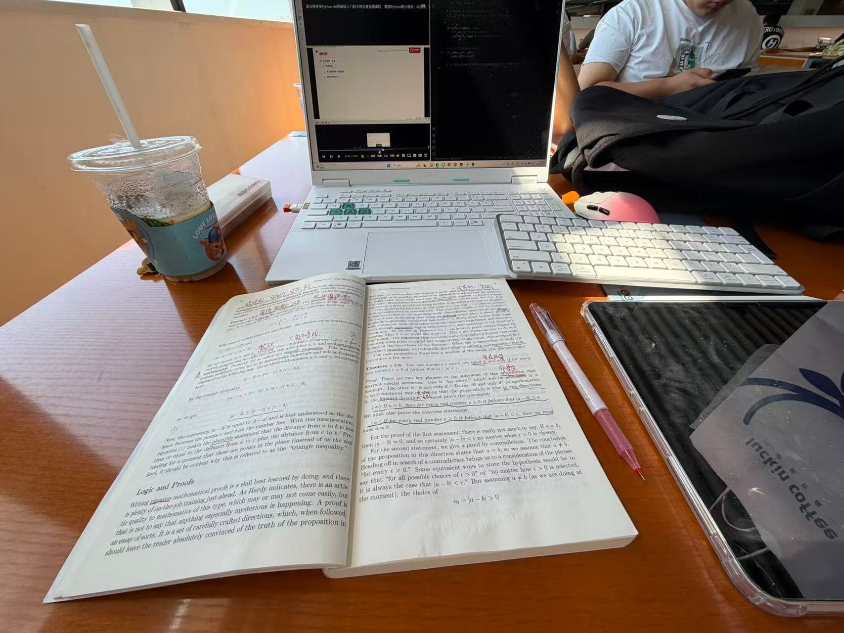 A laptop, mathematics textbook, keyboard, and handwritten annotations on a library desk