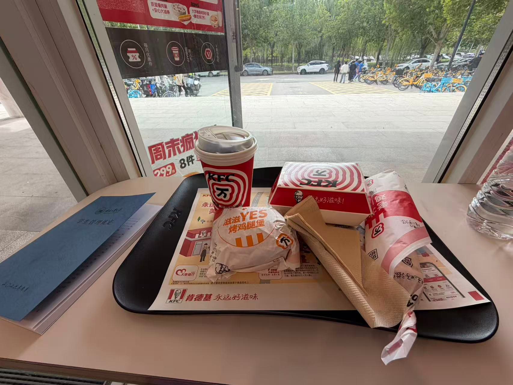 A burger, fries, coffee, and food boxes on a table beside a window