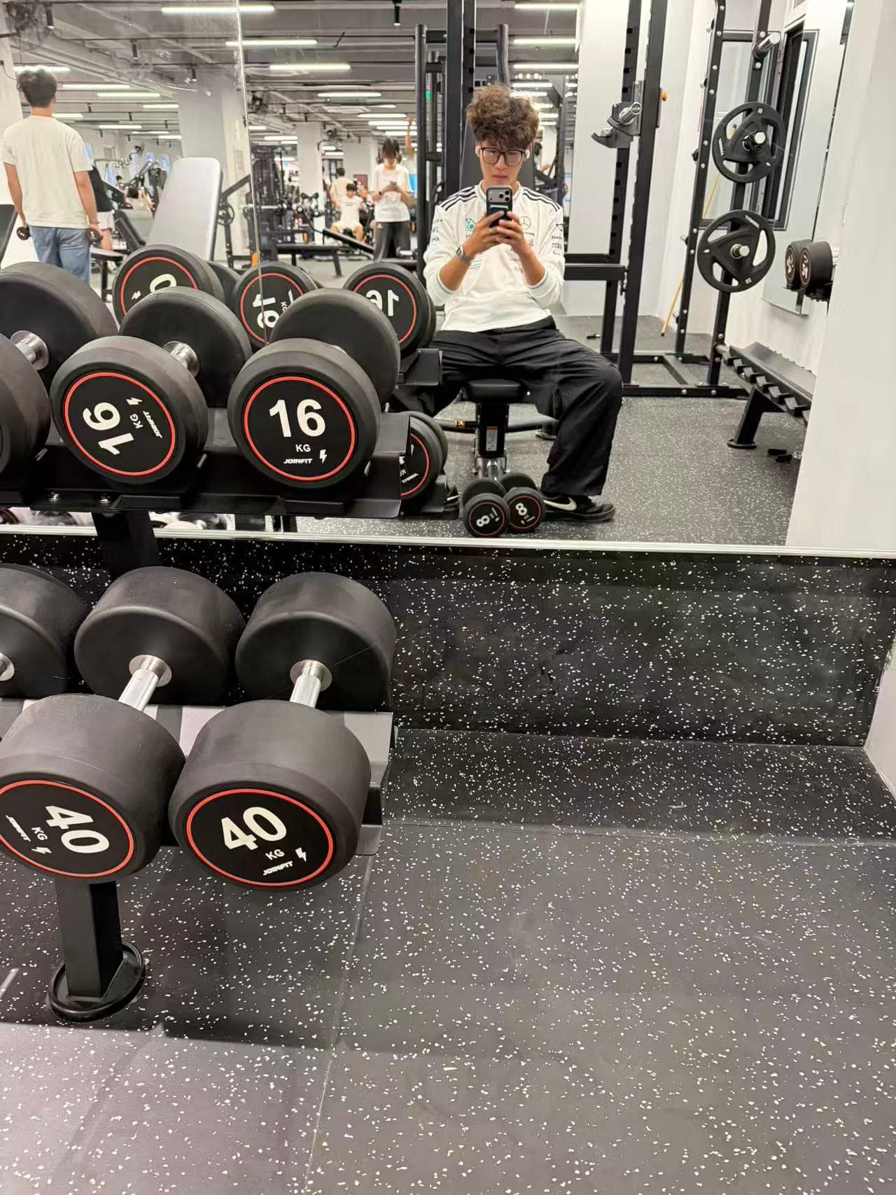 A mirror photo taken while sitting in front of the dumbbell rack at the gym