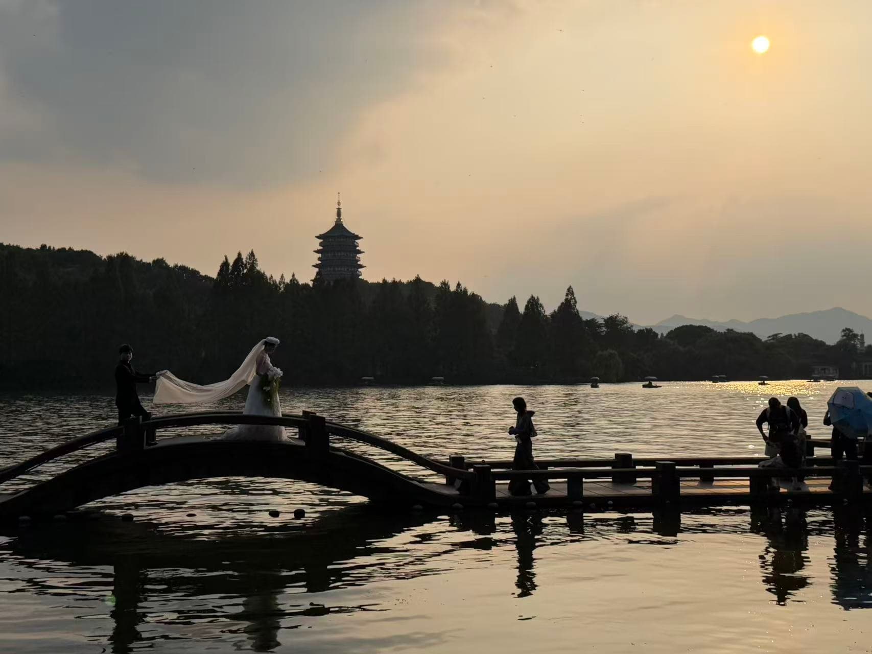 A lake at sunset, with an arched bridge and a distant tower