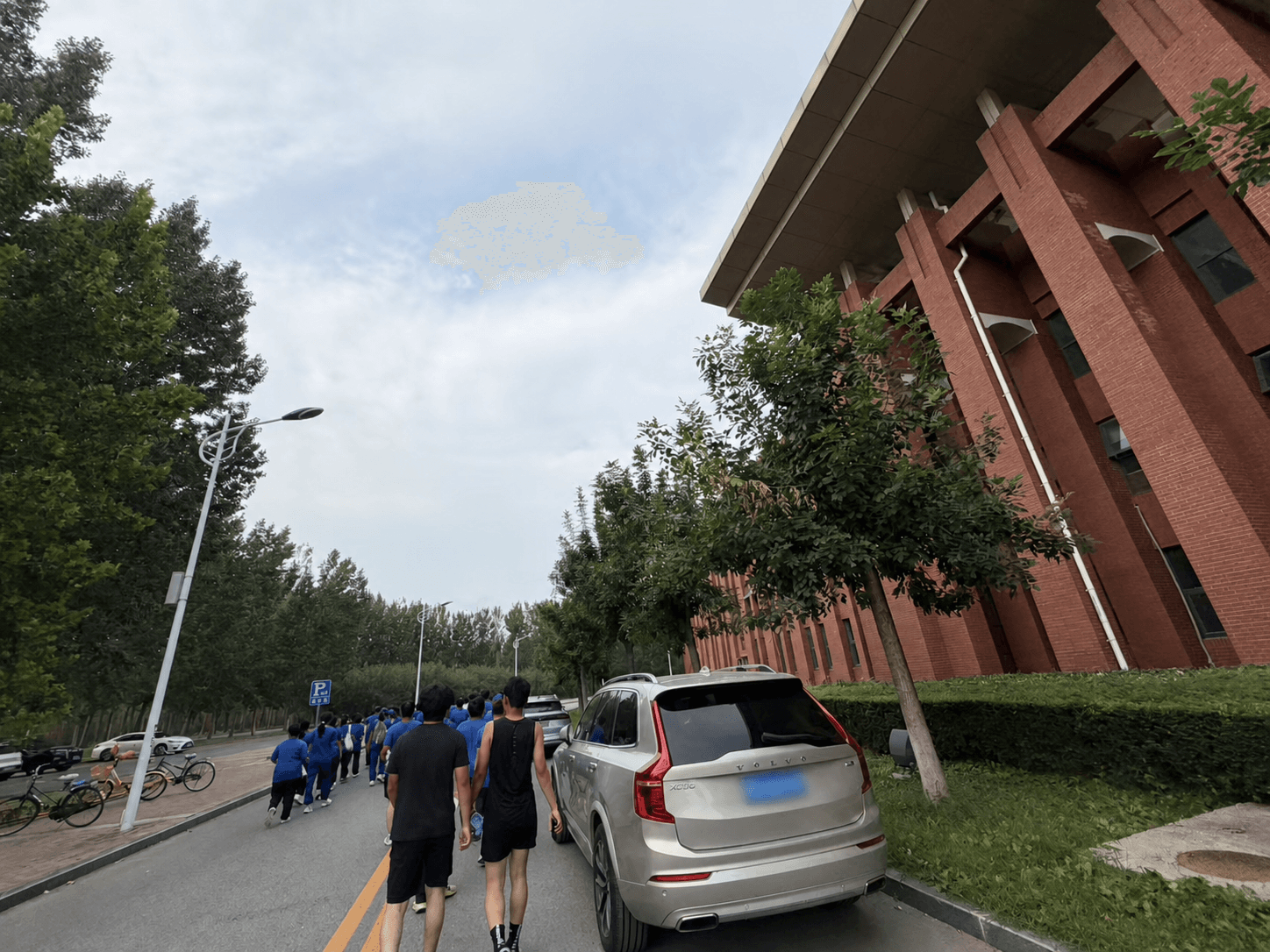 Students walking along a campus road after the fitness test, with the nearby car's plate blurred