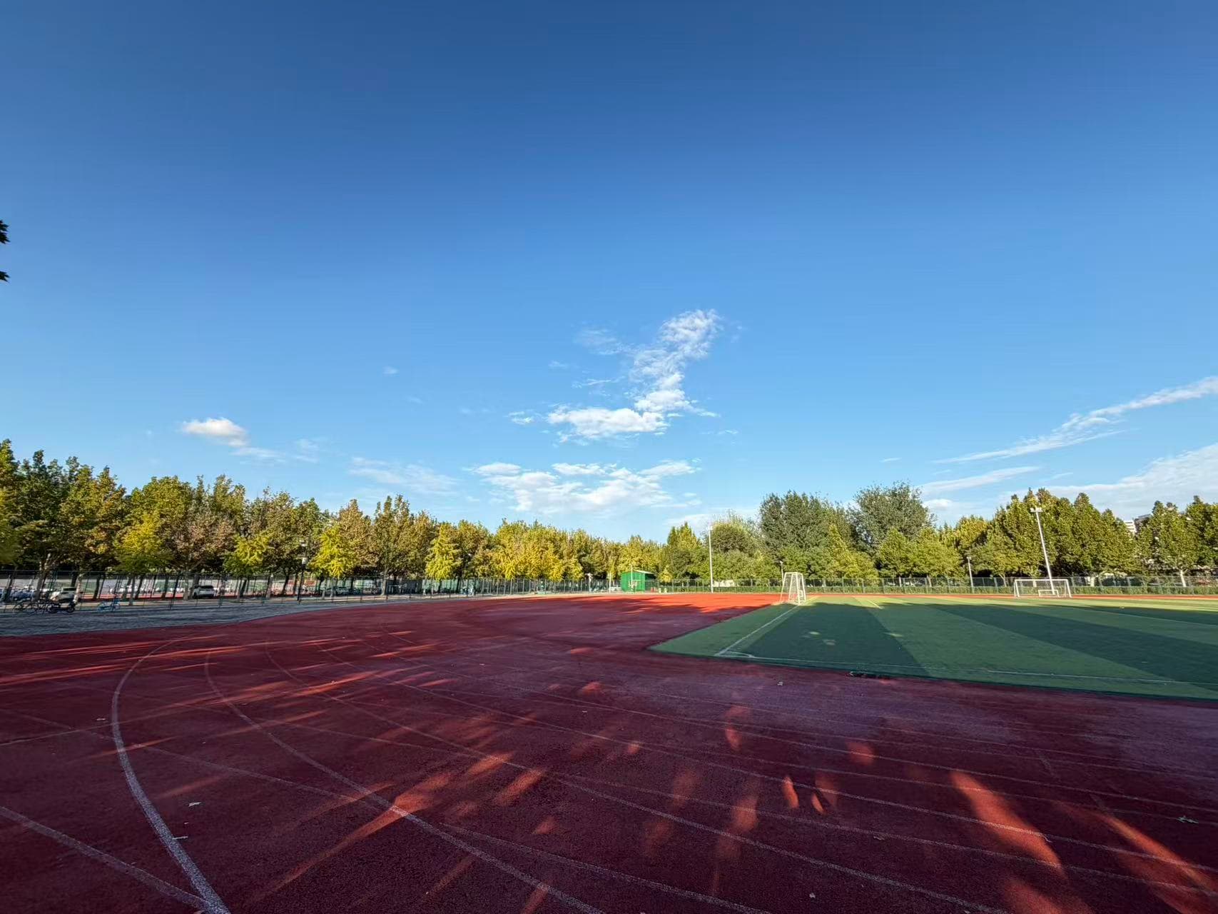 A school track and football field beneath a clear blue sky, with trees lit by the sun