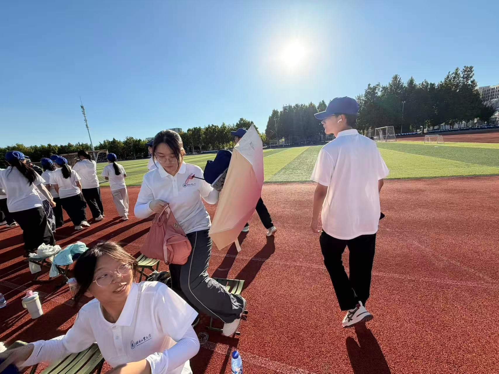 A sunlit athletics field with students taking a break from military training