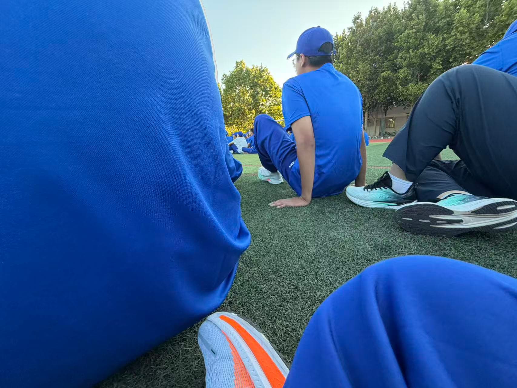Students in blue training uniforms sitting on the grass during a break