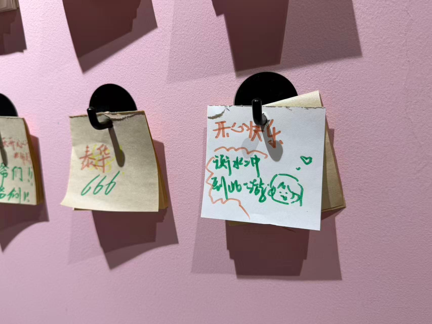 Handwritten wishes for happiness and a small smiling face on notes hanging against a pink wall