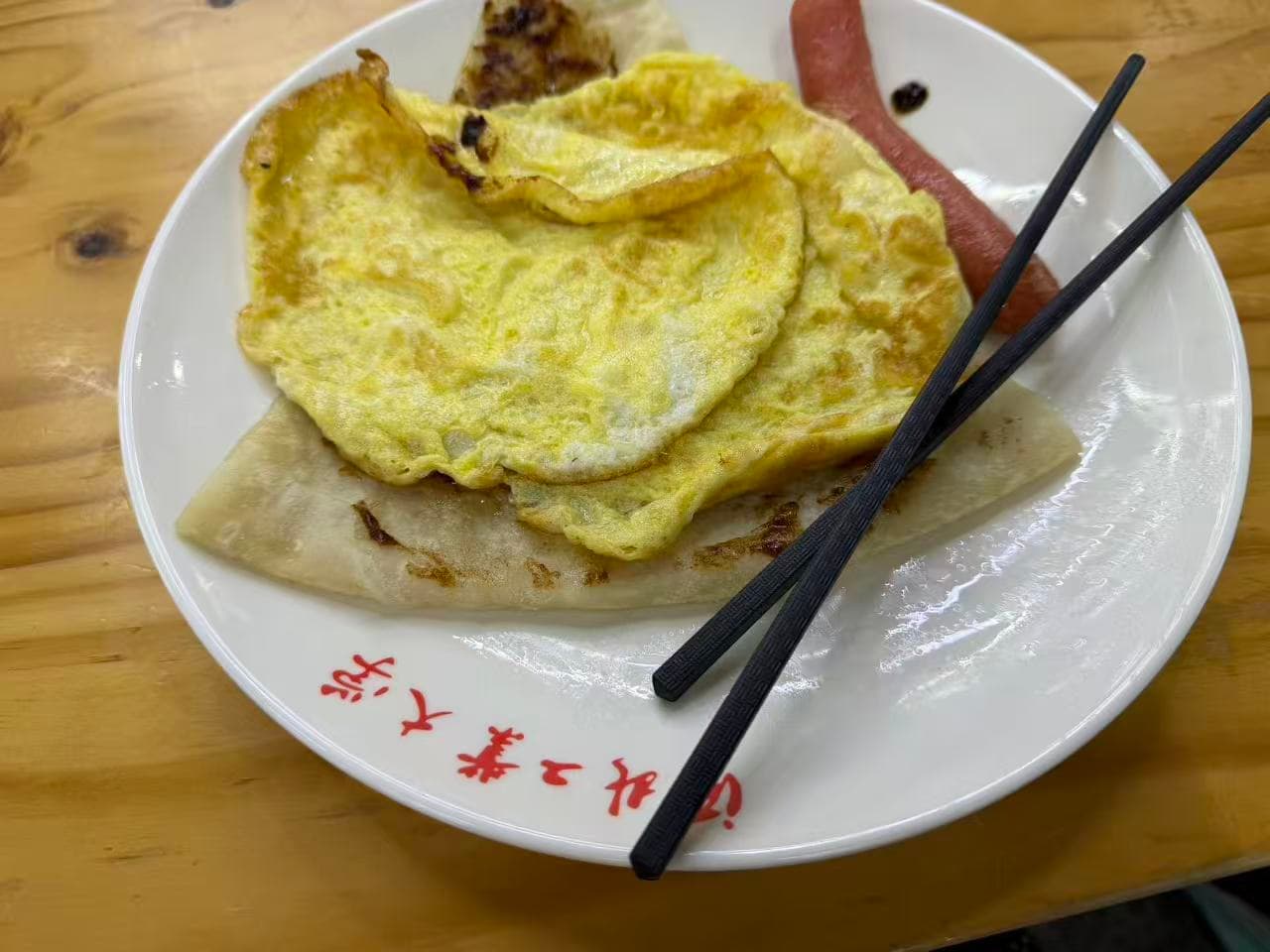 A simple meal of fried eggs, flatbread, and sausage on a wooden table