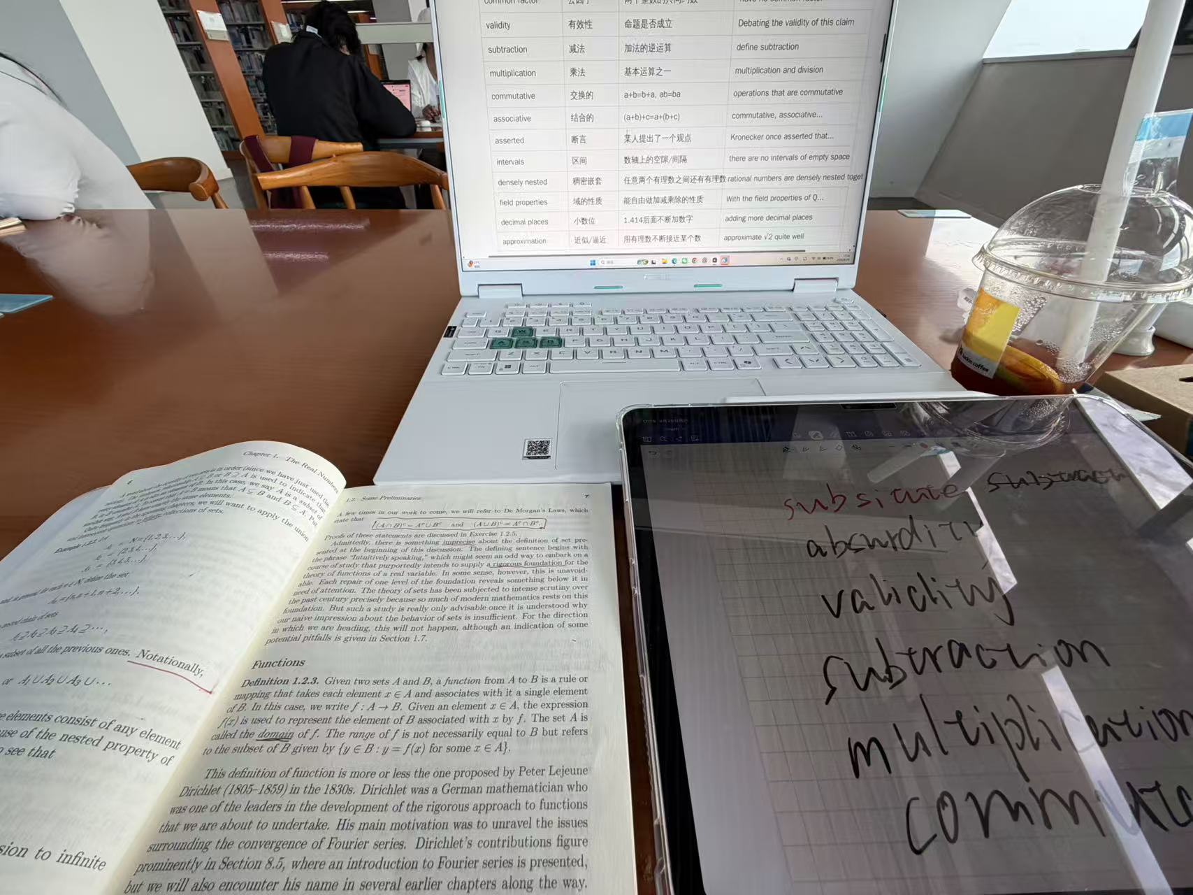 An analysis glossary on a computer beside an English textbook and handwritten vocabulary notes
