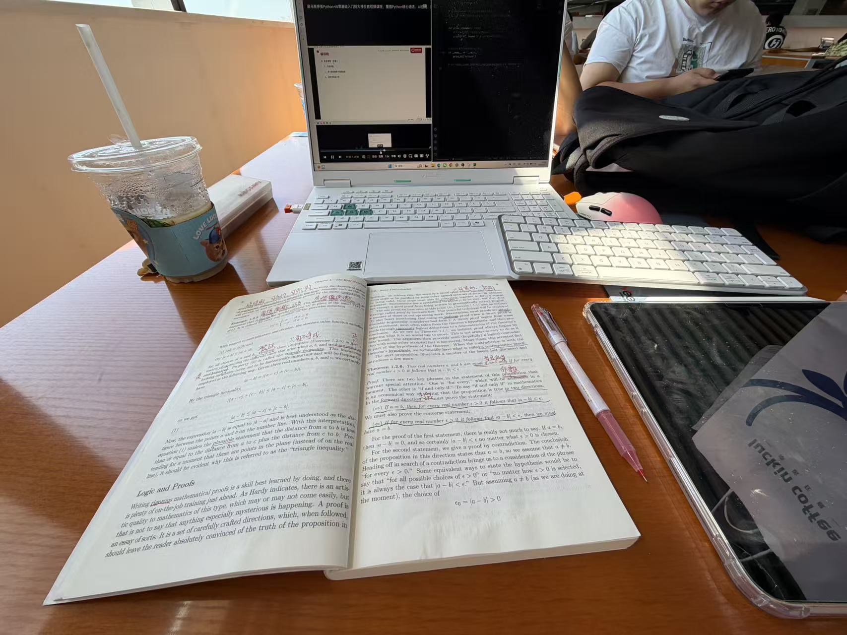 A laptop, mathematics textbook, keyboard, and handwritten annotations on a library desk