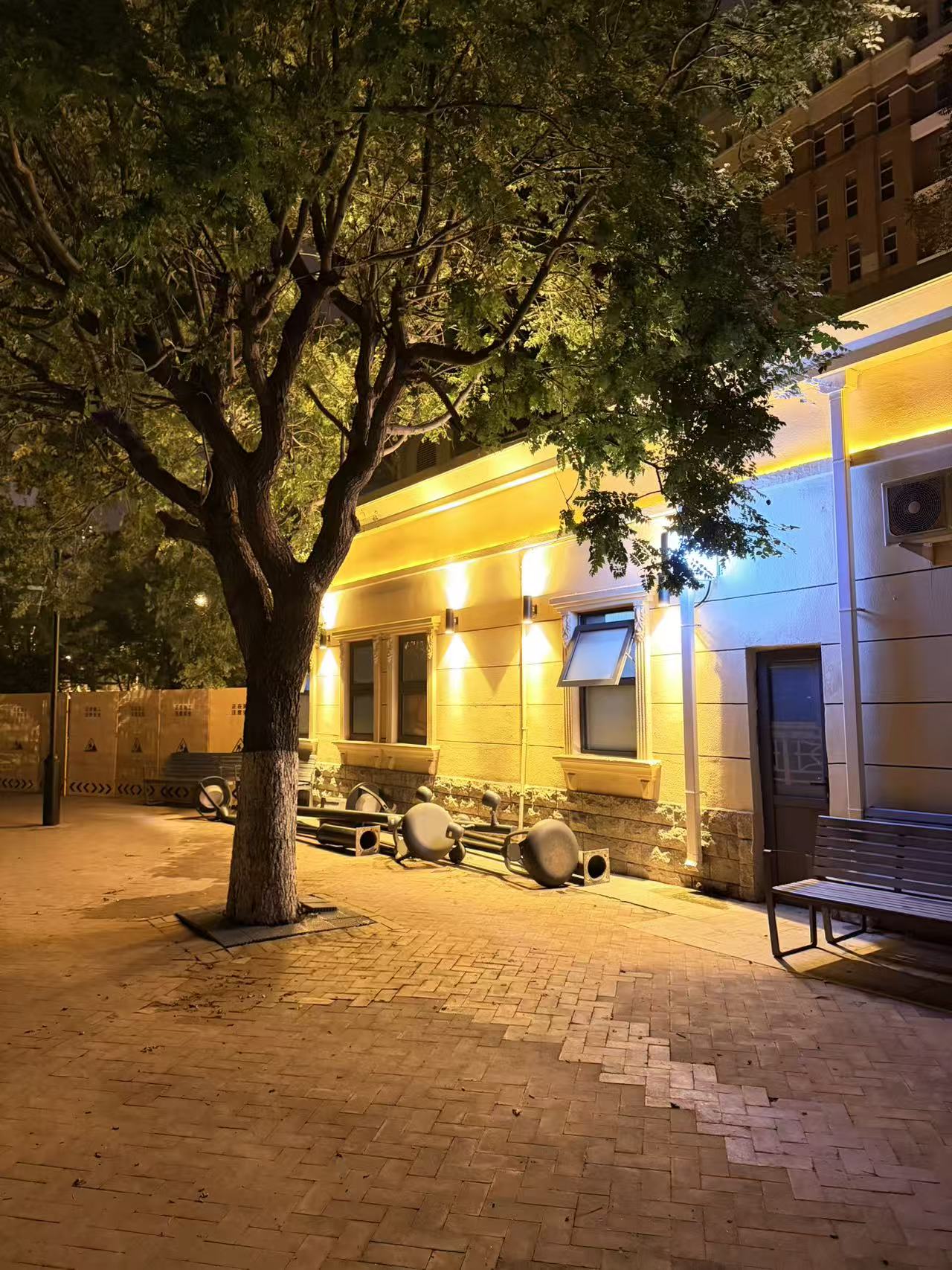 A quiet street, tree, and building under warm yellow lights late at night