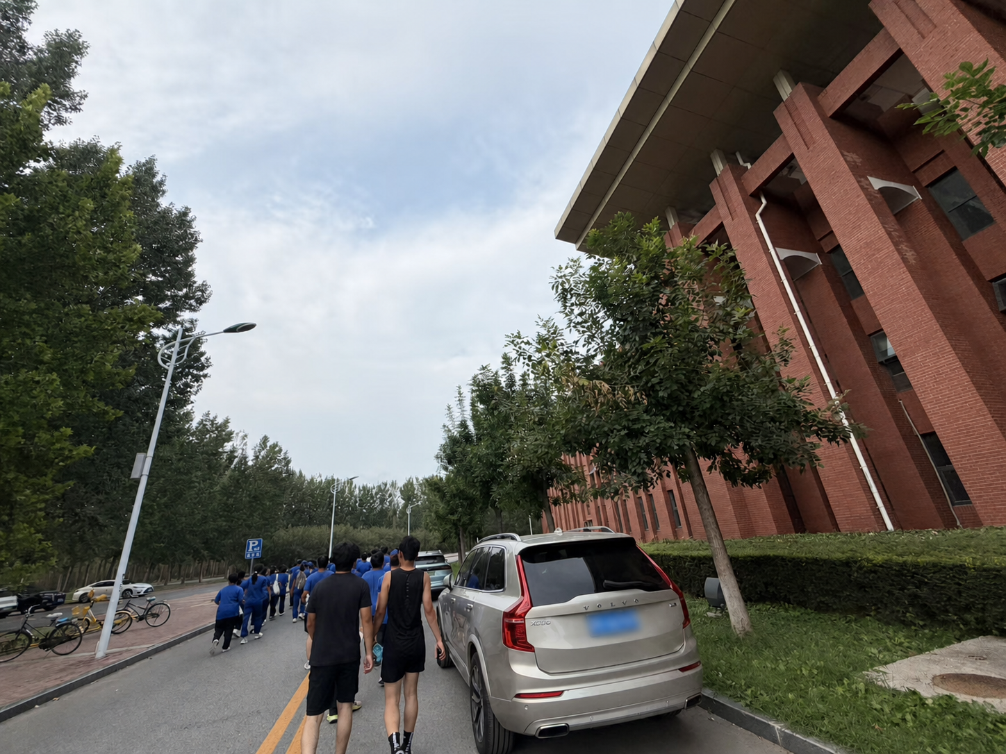 Students walking along a campus road after the fitness test, with the nearby car's plate blurred