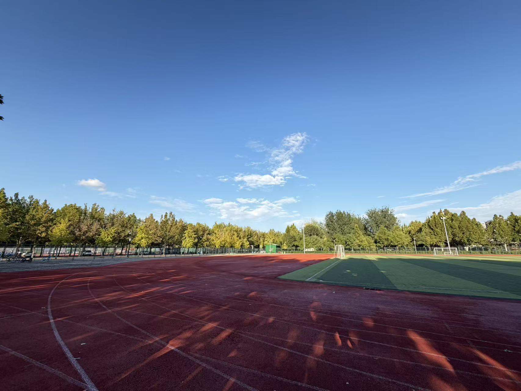 A school track and football field beneath a clear blue sky, with trees lit by the sun