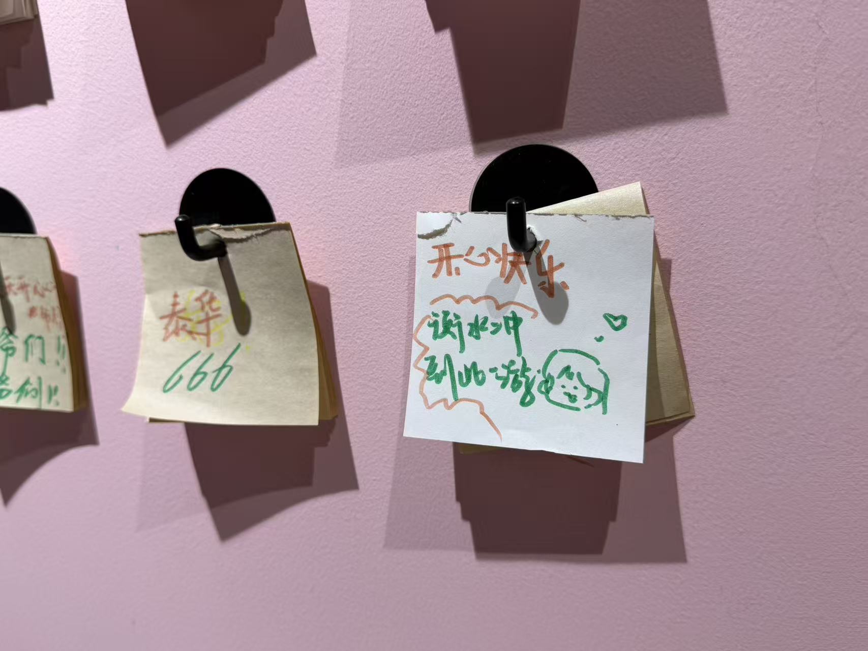 Handwritten wishes for happiness and a small smiling face on notes hanging against a pink wall