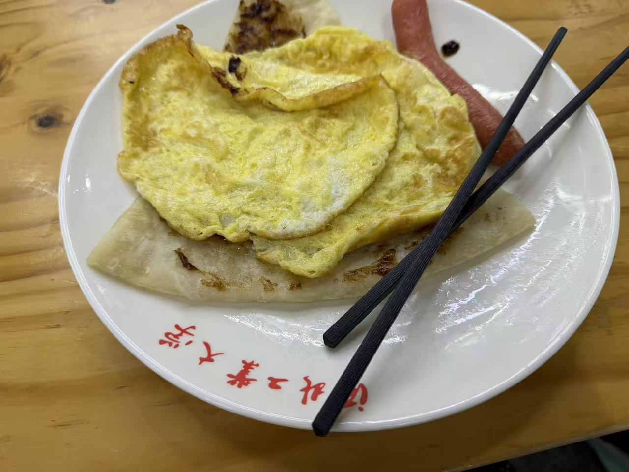 A simple meal of fried eggs, flatbread, and sausage on a wooden table
